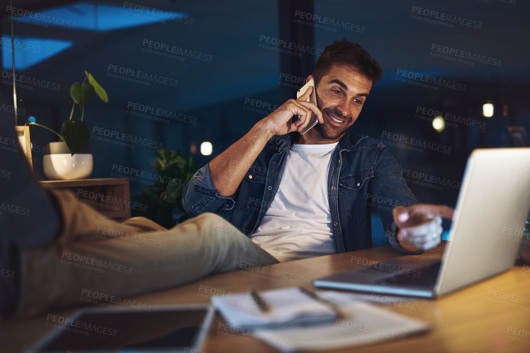 Buy stock photo Shot of a handsome young businessman talking on his cellphone while sitting at his desk in a modern office