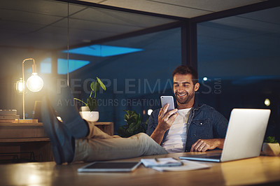 Buy stock photo Shot of a handsome young businessman using his cellphone while sitting at his desk in a modern office