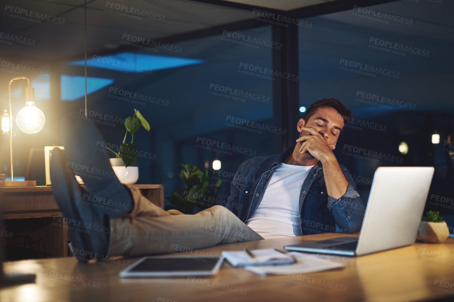 Buy stock photo Shot of a handsome young businessman falling asleep while working late at night in a modern office