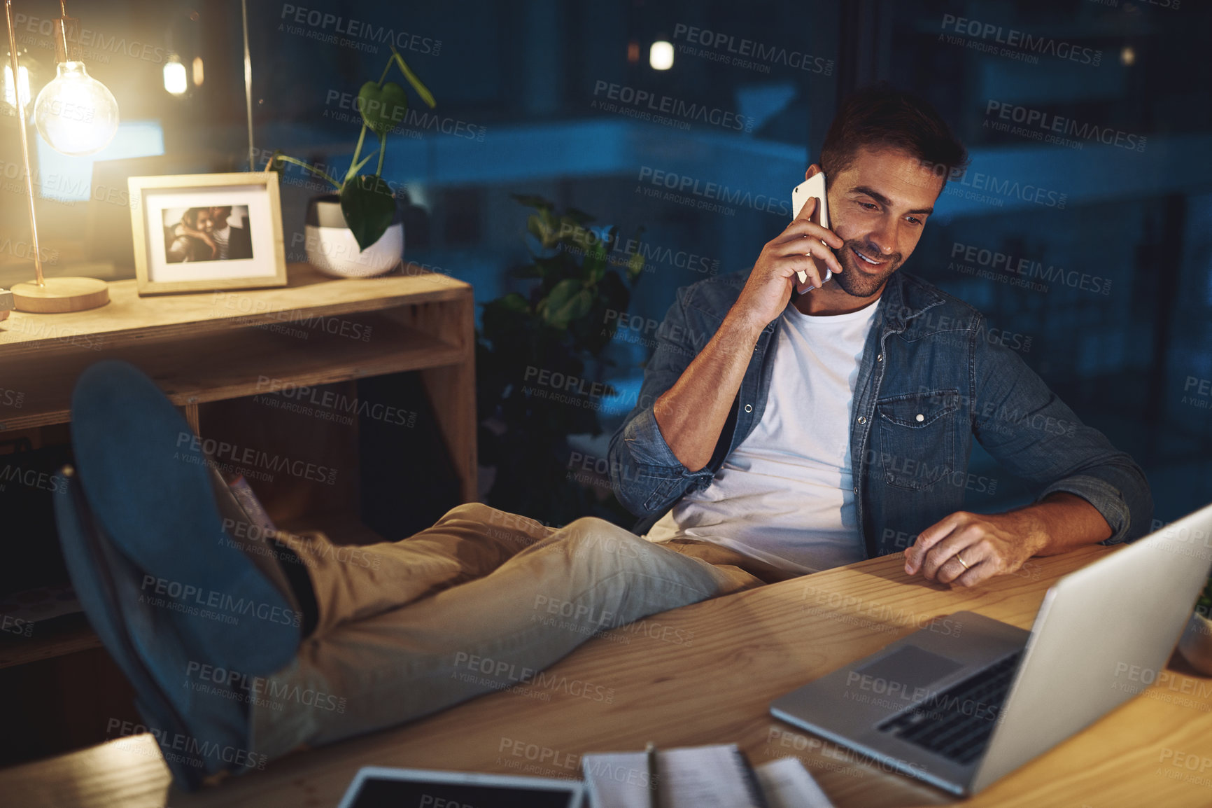 Buy stock photo Relax, desk and man in office with phone call, laptop and online chat for lead generation at digital agency. Late, night and designer with smartphone for networking, communication or business contact