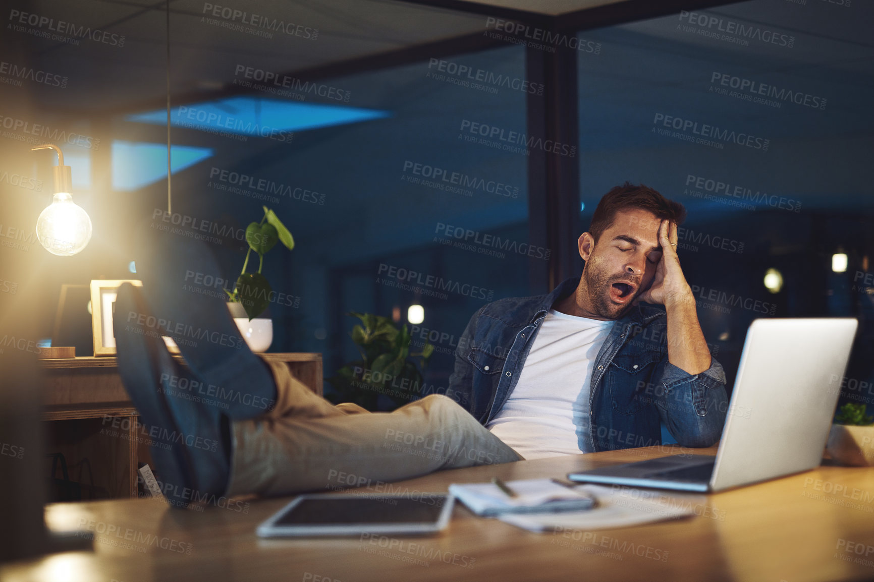 Buy stock photo Shot of a handsome young businessman falling asleep while working late at night in a modern office