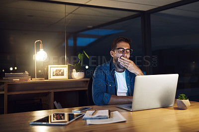 Buy stock photo Shot of a handsome young businessman yawning while working late at night in a modern office