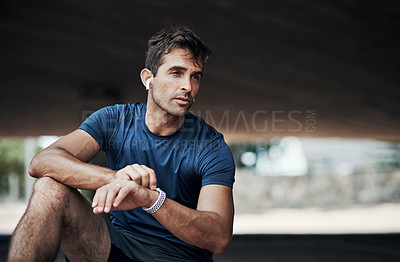 Buy stock photo Shot of a sporty young man checking his watch while exercising outdoors