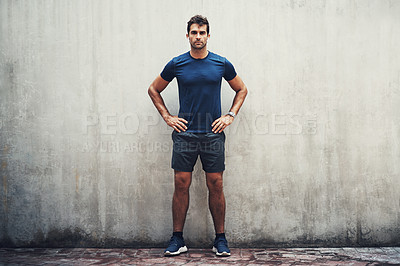 Buy stock photo Portrait of a sporty young man standing against a grey wall while exercising outdoors