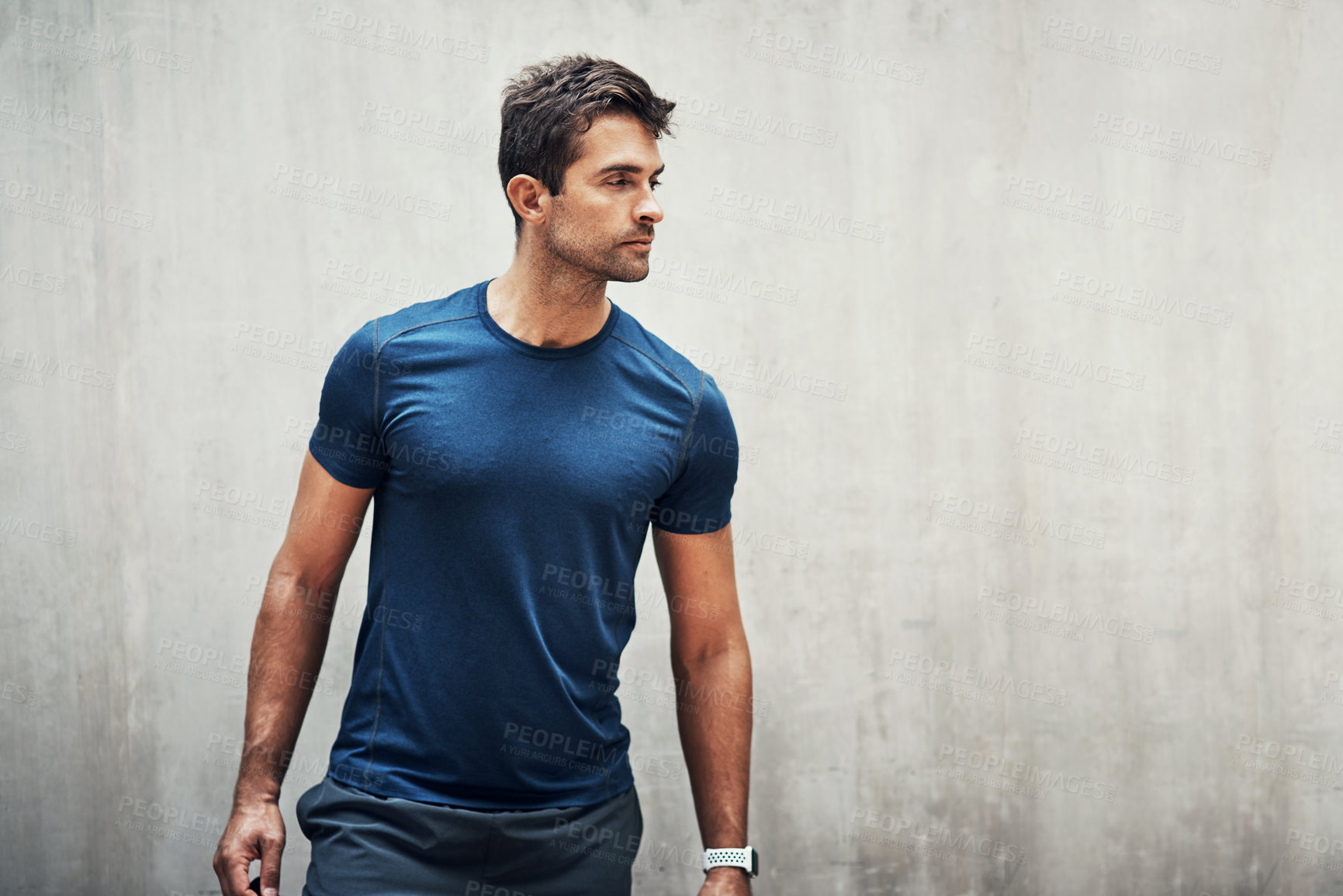 Buy stock photo Shot of a sporty young man standing against a grey wall while exercising outdoors