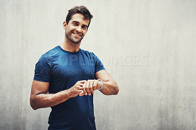 Buy stock photo Portrait of a sporty young man checking his watch while exercising outdoors
