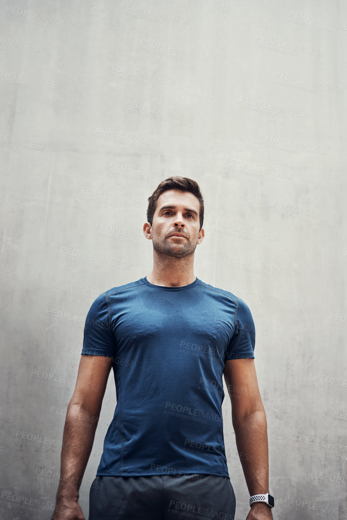 Buy stock photo Shot of a sporty young man standing against a grey wall while exercising outdoors