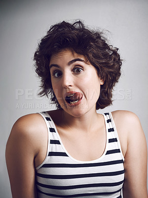 Buy stock photo Studio portrait of an attractive young woman making a funny face with her tongue while standing against a grey background