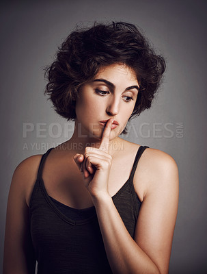 Buy stock photo Studio shot of an attractive young woman with her finger over her lips against a grey background