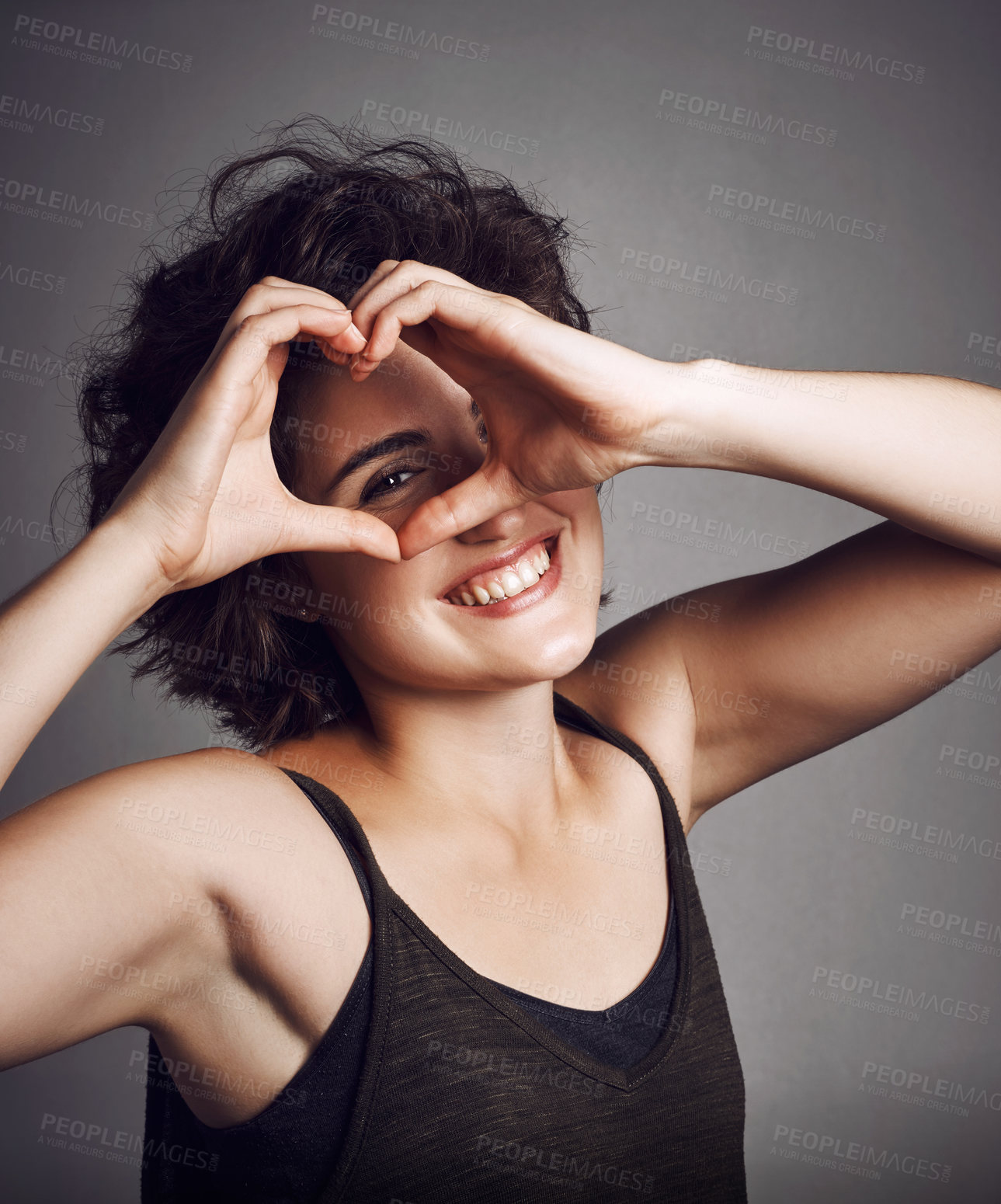 Buy stock photo Studio portrait of an attractive young woman making a heart shape on her eye against a grey background