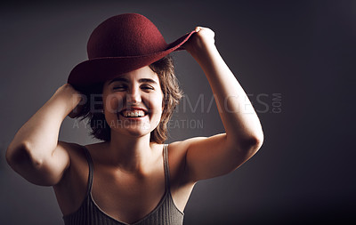 Buy stock photo Stdio shot of an attractive young woman smiling while adjusting her hat against a grey background