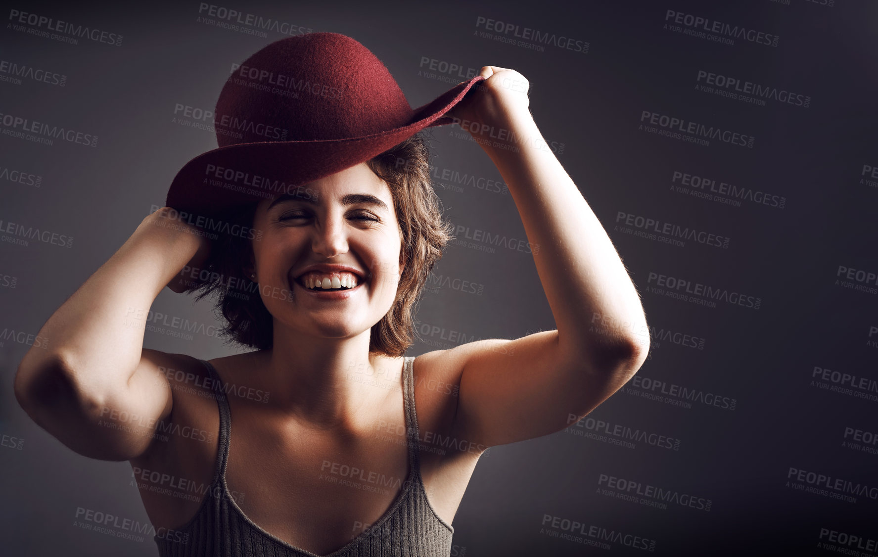 Buy stock photo Stdio shot of an attractive young woman smiling while adjusting her hat against a grey background