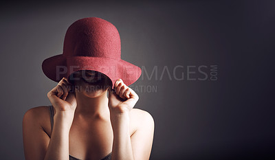 Buy stock photo Studio shot of an unrecognizable young woman covering her face with a hat against a grey background