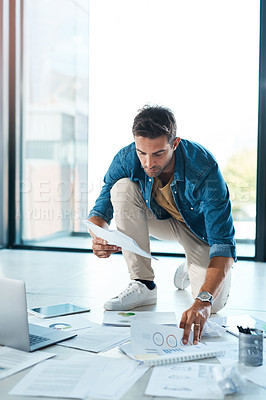 Buy stock photo Shot of a young businessman brainstorming with paperwork on a floor in an office