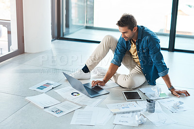 Buy stock photo Shot of a young businessman brainstorming with a laptop and paperwork on a floor in an office