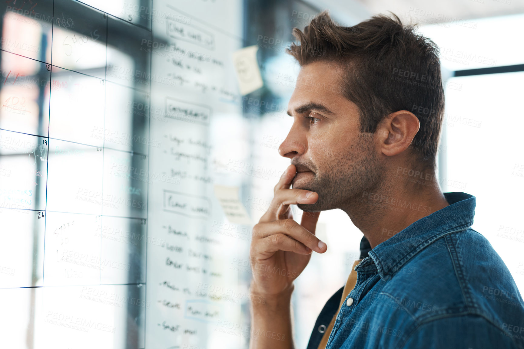 Buy stock photo Shot of a young businessman brainstorming with notes on a glass wall in an office