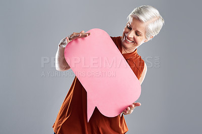 Buy stock photo Shot of a cheerful mature woman holding a speech bubble against a grey background