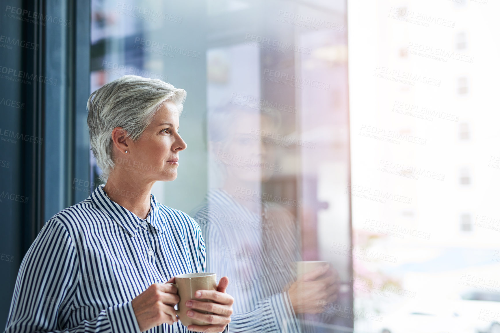 Buy stock photo Shot of an attractive mature businesswoman drinking coffee while looking out of her office window