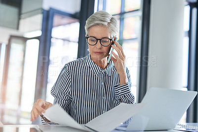 Buy stock photo Shot of an attractive mature businesswoman  handling paperwork while taking a phone call at her office desk at work