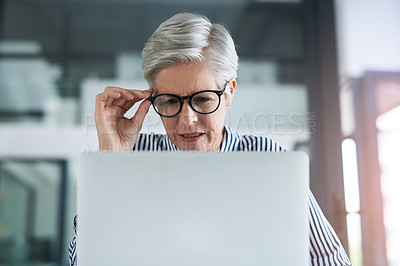 Buy stock photo Shot of an attractive mature businesswoman adjusting her glasses while working on  a laptop in her office