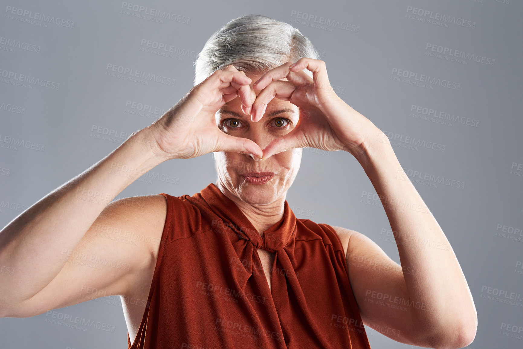 Buy stock photo Portrait of an attractive mature woman making a heart shape with her hands against a grey background