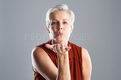 Buy stock photo Portrait of an attractive mature woman blowing kisses against a grey background