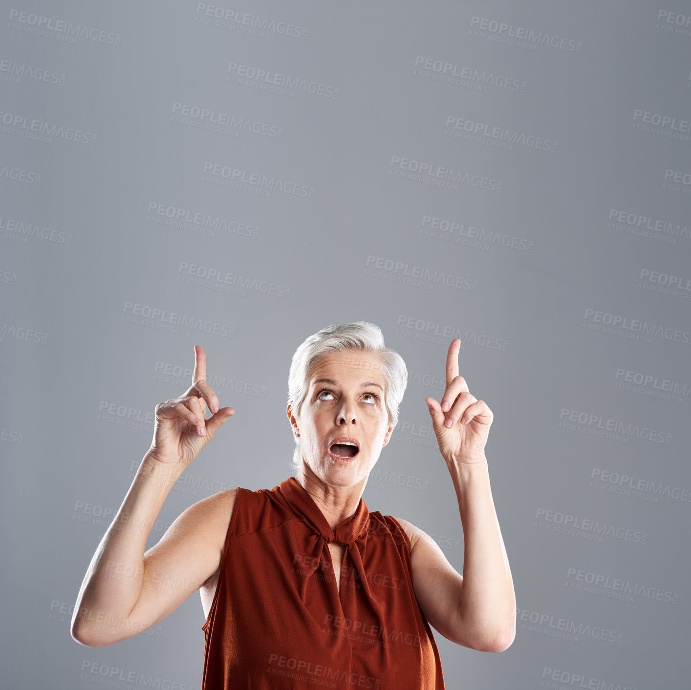 Buy stock photo Shot of a cheerful mature woman looking and pointing up against a grey background