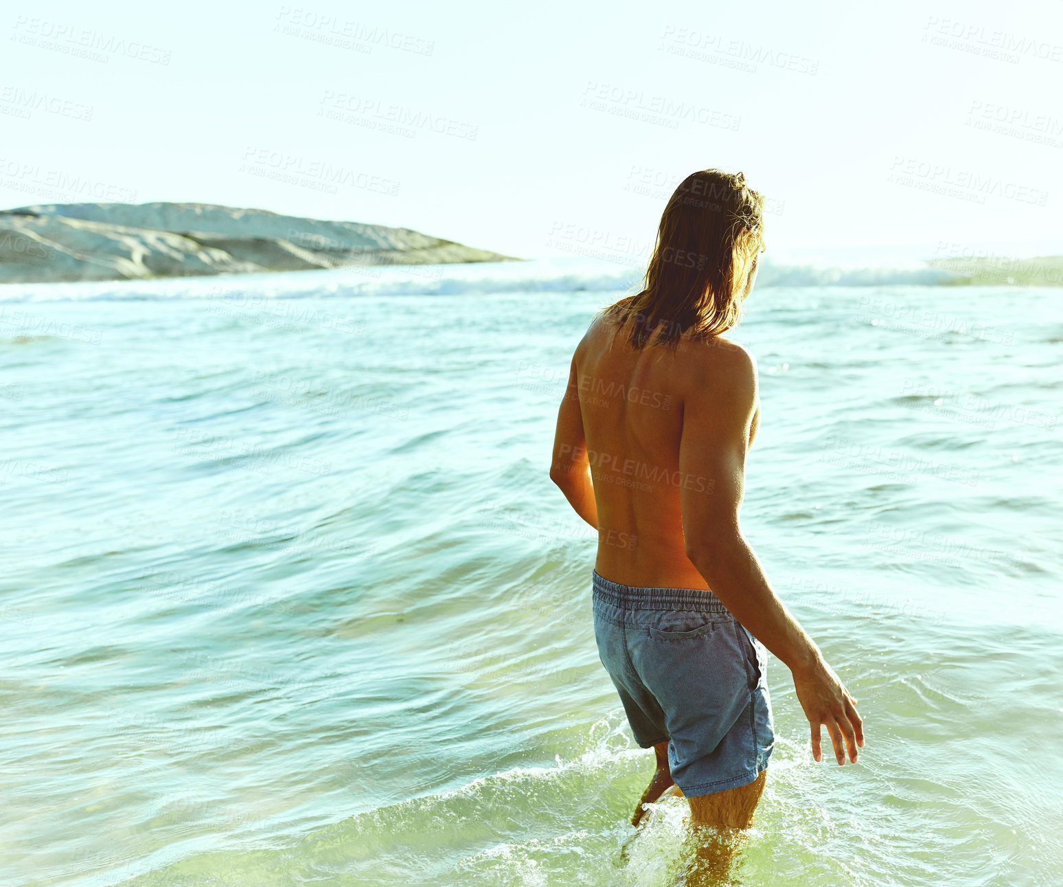 Buy stock photo Rearview shot of a handsome young man standing in the water at the beach