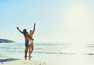 Buy stock photo Rearview shot of a young couple cheering while enjoying some quality time together at the beach