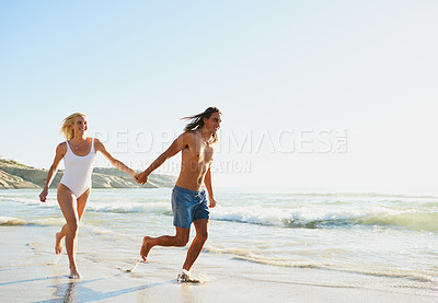 Buy stock photo Shot of a young couple running along the beach