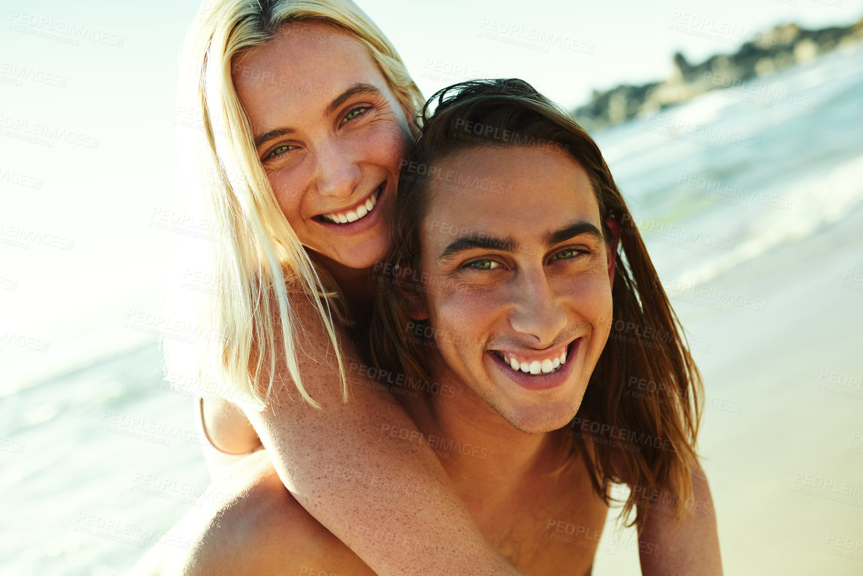 Buy stock photo Portrait of a young man giving his girlfriend a piggyback ride at the beach