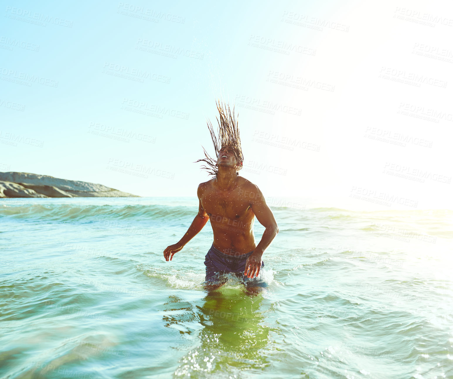 Buy stock photo Shot of a handsome young man flipping his hair while standing in the water at the beach
