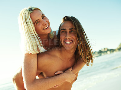 Buy stock photo Shot of a young man giving his girlfriend a piggyback ride at the beach