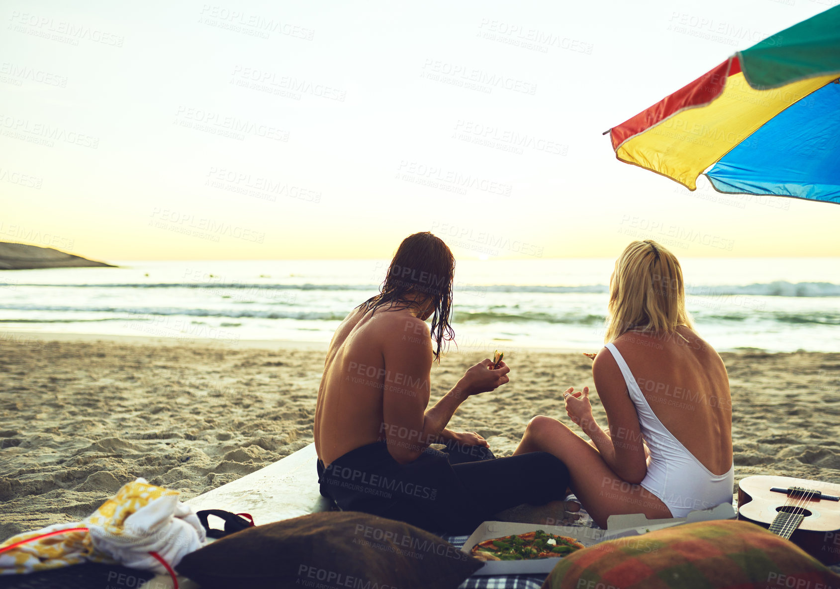 Buy stock photo Rearview shot of a young unrecognizable couple having a small picnic date on the beach at sunset