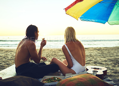 Buy stock photo Rearview shot of a young unrecognizable couple having a small picnic on the beach at sunset