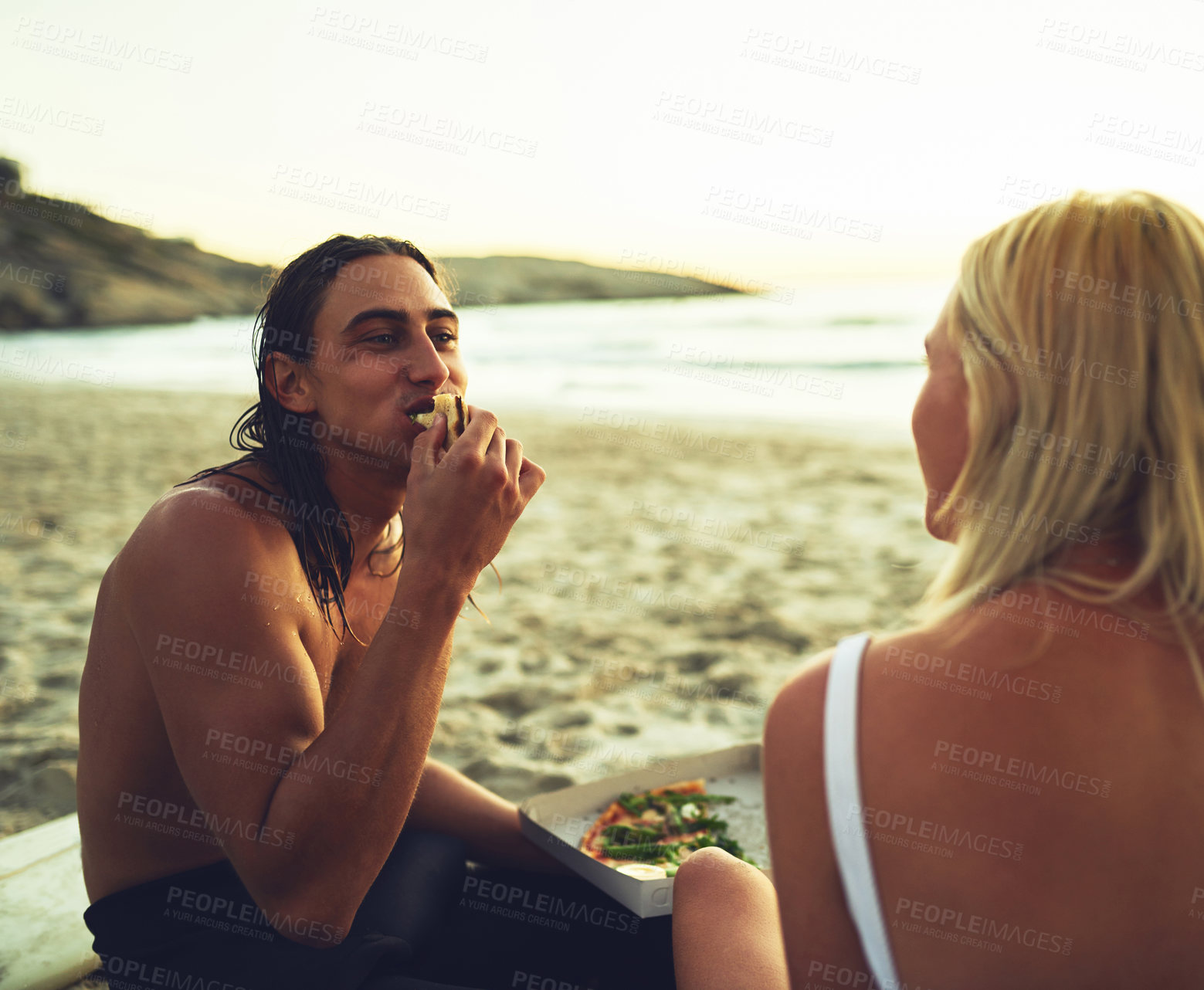 Buy stock photo Shot of an affectionate young couple having a picnic date and eating on the beach at sunset