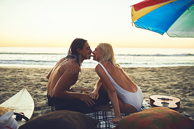 Buy stock photo Rearview shot of a young affectionate couple having a picnic date and sharing a pizza slice on the beach at sunset