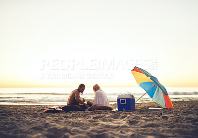 Buy stock photo Shot of an affectionate young couple having a picnic date on the beach at sunset