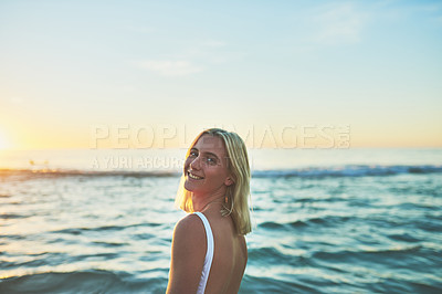 Buy stock photo Cropped portrait of an attractive young female smiling over her shoulder on the beach at sunset