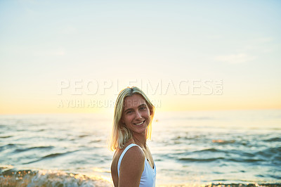 Buy stock photo Cropped portrait of an attractive young female smiling over her shoulder on the beach at sunset