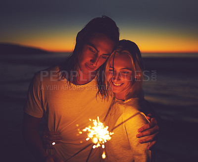 Buy stock photo Night, beach and couple with sparklers for holiday, vacation and celebrate new year together. Smile, man and woman with fireworks by sea for romantic date, travel and hug for love outdoor at sunset