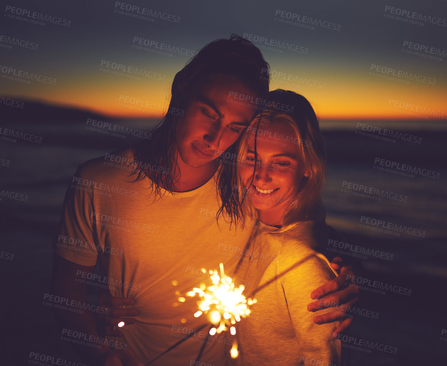 Buy stock photo Night, beach and couple with sparklers for holiday, vacation and celebrate new year together. Smile, man and woman with fireworks by sea for romantic date, travel and hug for love outdoor at sunset