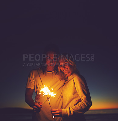 Buy stock photo Shot of a young couple playing with sparklers on the beach at night