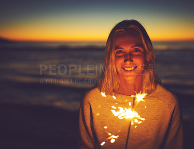 Buy stock photo Portrait of a young woman holding a sparkler at the beach at night