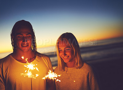 Buy stock photo Shot of a young couple playing with sparklers on the beach at night