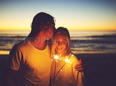 Buy stock photo Shot of a young couple playing with sparklers on the beach at night