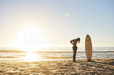Buy stock photo Full length shot of an unrecognizable young man putting on his wetsuit before going surfing at sunset