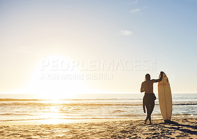 Buy stock photo Rearview shot of an unrecognizable young man holding his surfboard and looking out at the sea at sunset