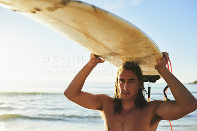 Buy stock photo Cropped portrait of a handsome young man carrying his surfboard over his head on the beach at sunset