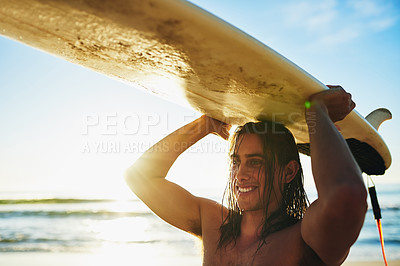 Buy stock photo Cropped shot of a handsome young man smiling while carrying his surfboard over his head on the beach at sunset